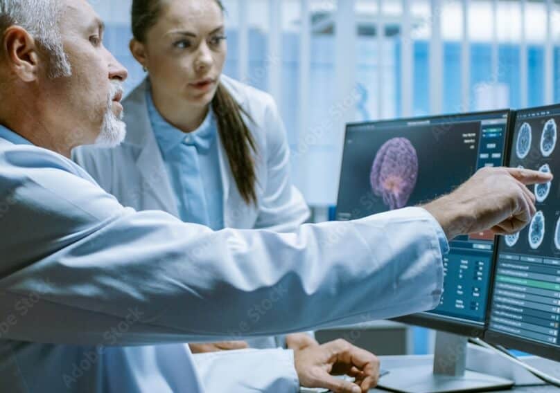 Two people look at data on a dual external monitor setup