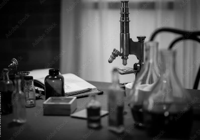 A microscopel, bottles, flasks and other equipment on a desk